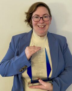 Photo of CLASI attorney Marissa Band holding the 2024 David Lynch Award (a glass trophy) from the University of Delaware's Center for Disabilities Studies.